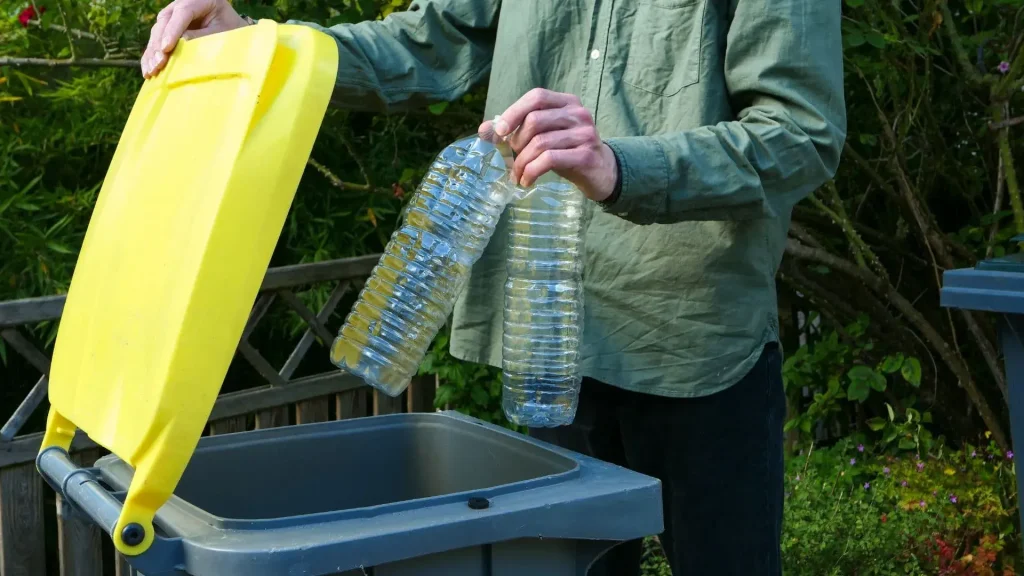 Un homme jette des bouteilles plastiques dans une poubelle